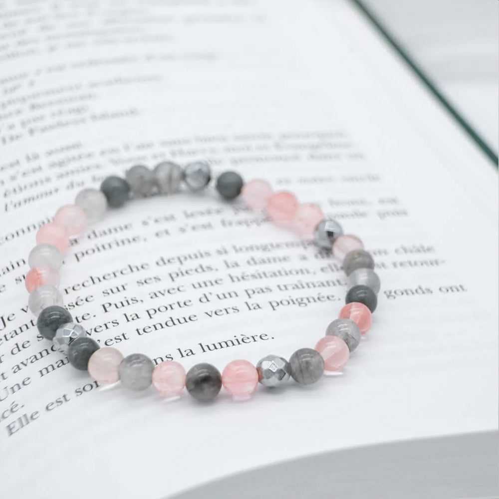 
                  
                    Bracelet de couleur rose et gris déposé sur un livre
                  
                