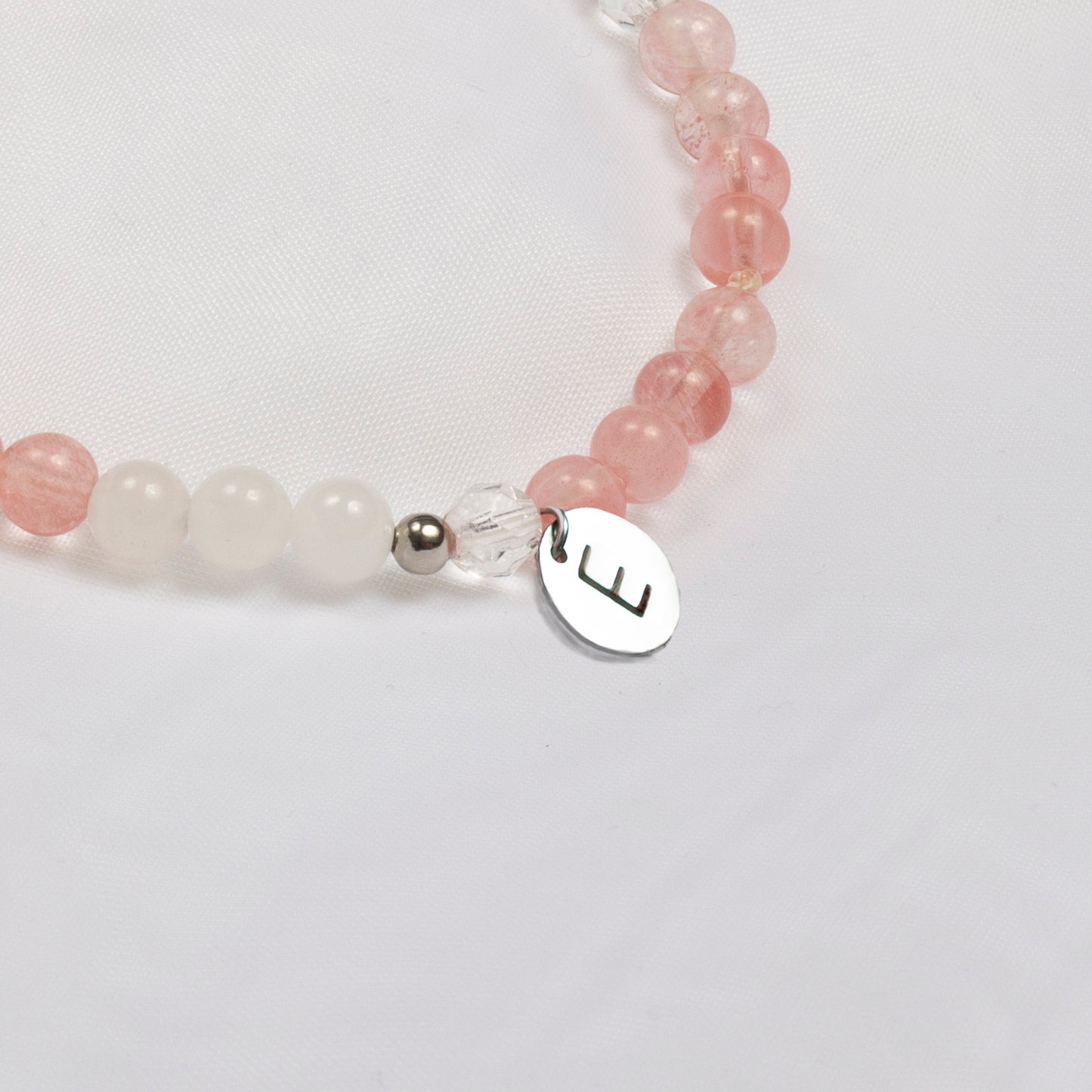 Breloque personnalisée de l'initiale E montée sur un bracelet de pierres fines transparentes et rosés. 