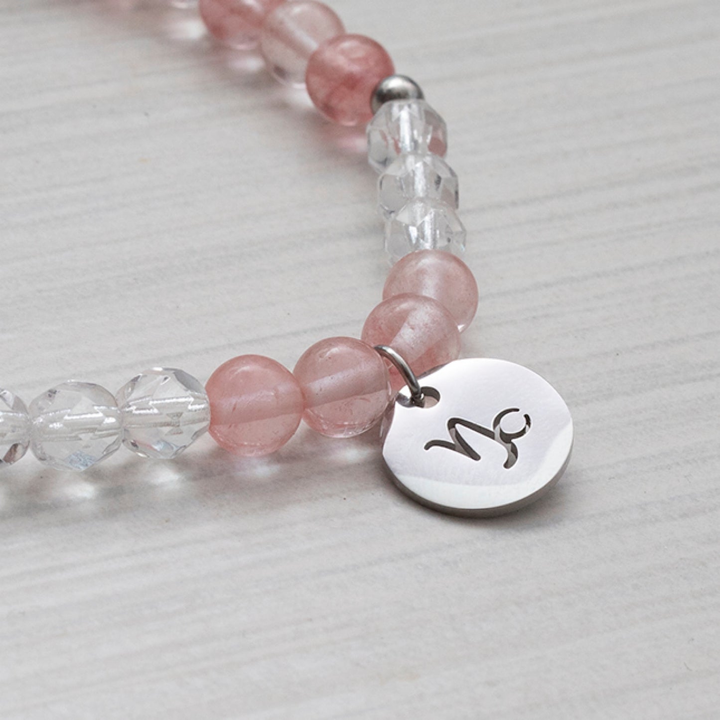 Breloques signes astrologiques sur un bracelet de pierres transparentes et roses