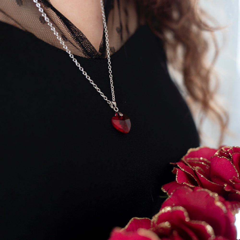 Femme aux vêtements noirs arborant le collier Valentine une chaîne en acier inoxydable et un pendentif en forme de cœur en cristal de Swarovski rouge 