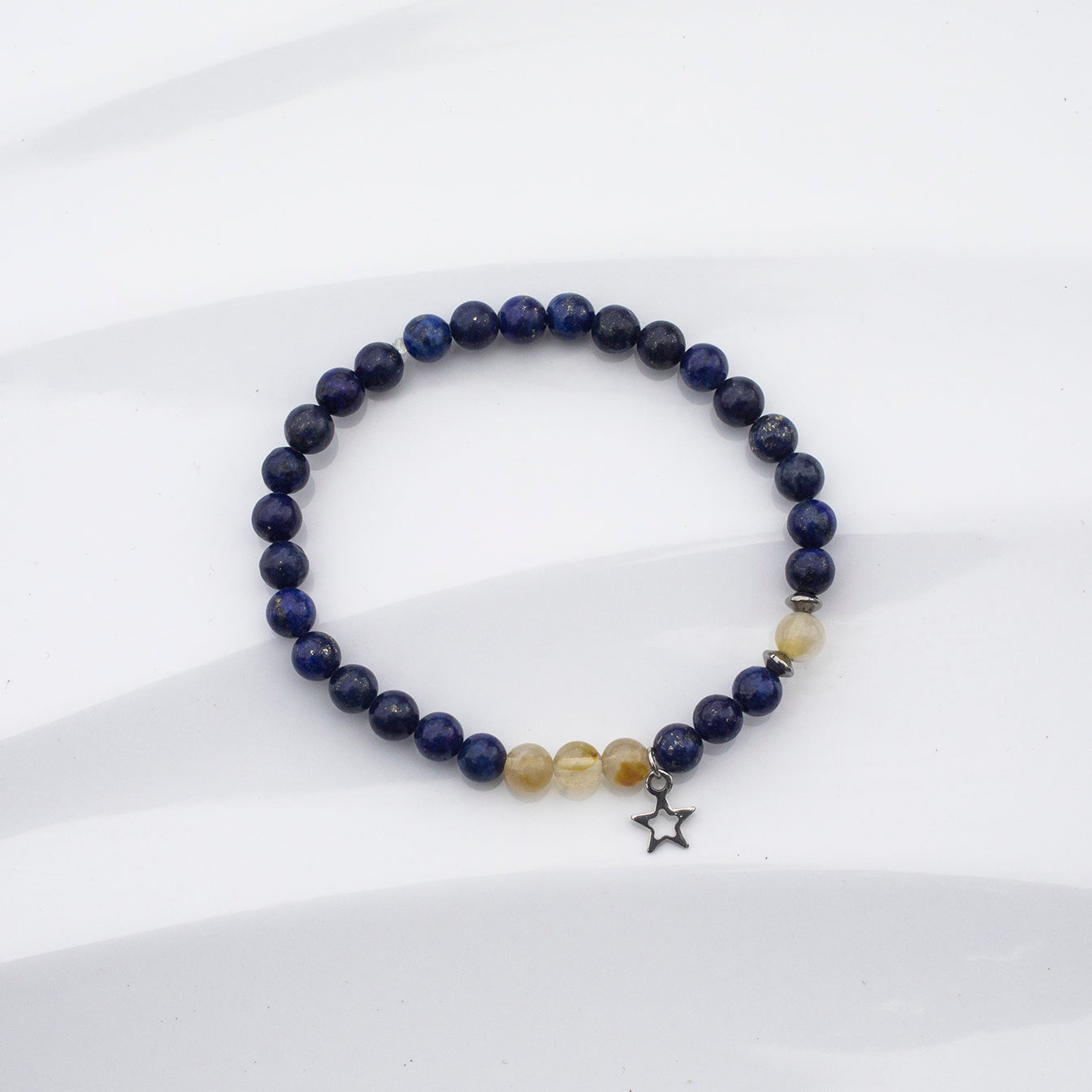Bracelet de couleur noir avec des pierres de lapis lazuli et de fines quartz beige. Breloque en étoile sur fond blanc