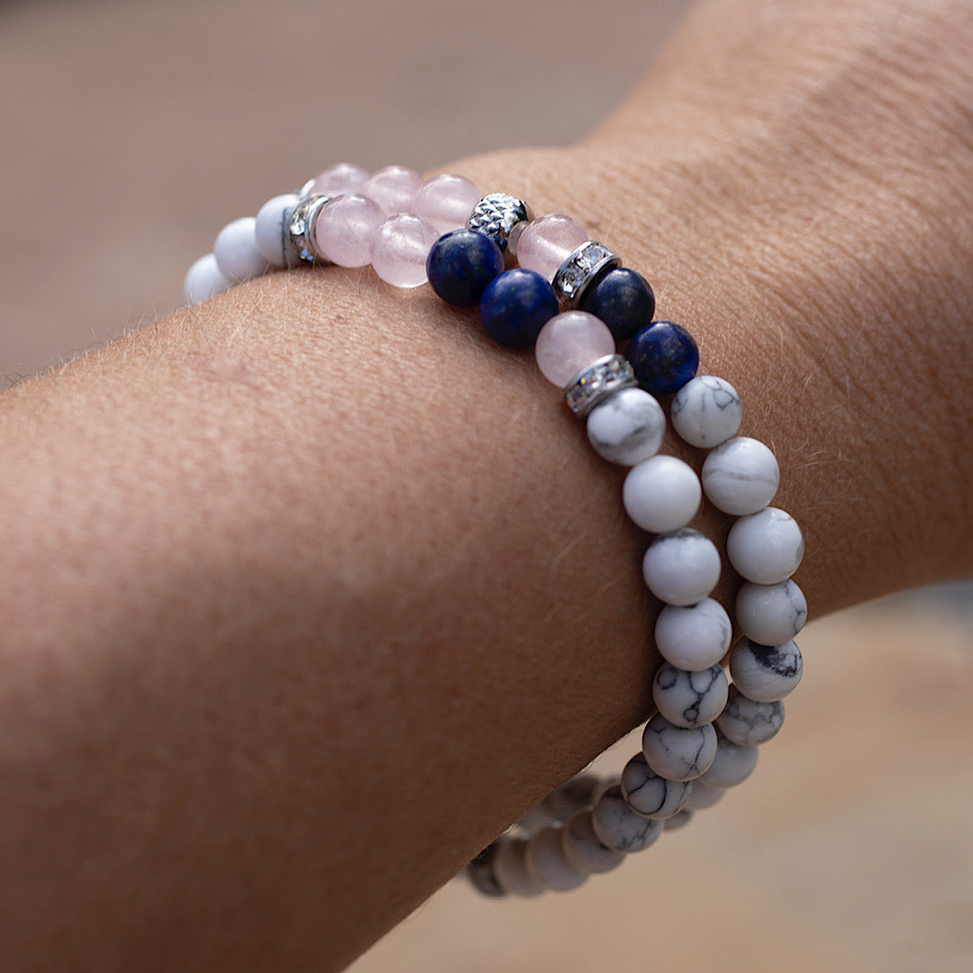Poignet de femme arborant le duo de bracelets élastiques faits avec des pierres fines howlite, quartz rose et lapis lazuli.