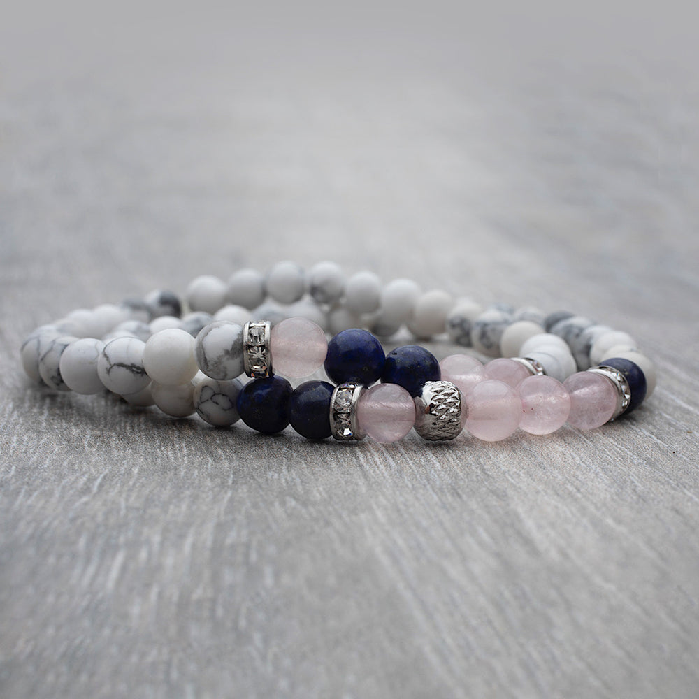 
                      
                        Duo de bracelets élastiques faits avec des pierres fines howlite, quartz rose et lapis lazuli déposé sur une table de bois.
                      
                    