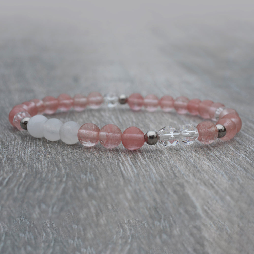 Bracelet de quartz rose et de jade blanc déposé sur une table en bois