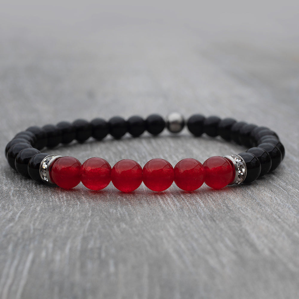 
                  
                    Bracelet composé d’onyx noir et de jade rouge déposé sur une table de bois
                  
                