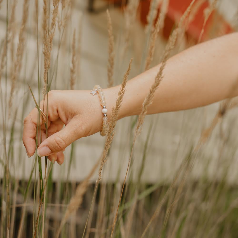 
                  
                    Poignet de femme dans la nature arborant un bracelet de quartz beige
                  
                
