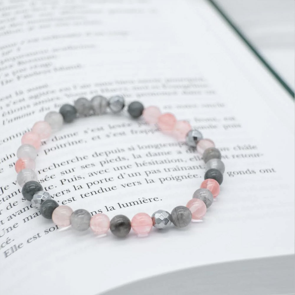 
                      
                        Bracelet de couleur rose et gris déposé sur un livre
                      
                    