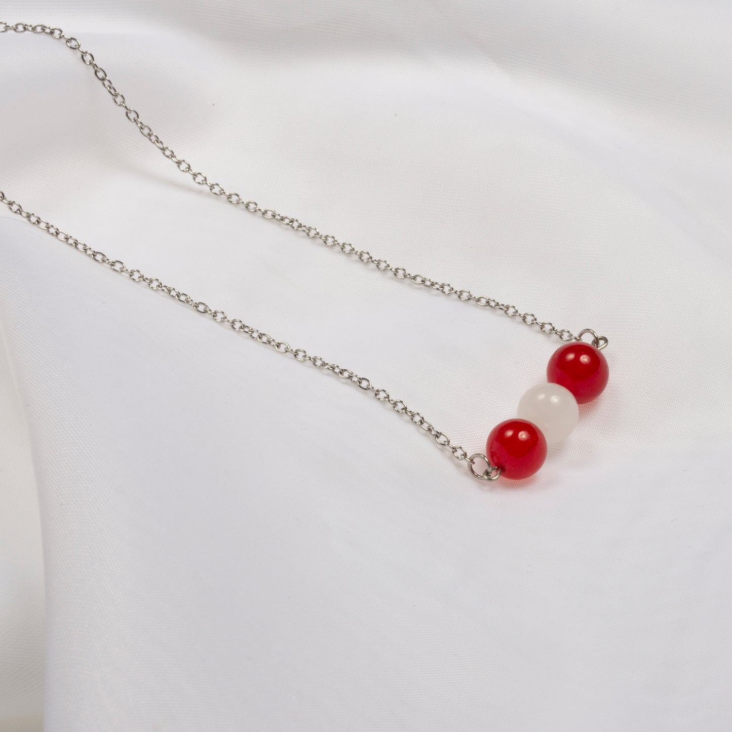 Joli collier composé de pierres fines jade rouge et jade blanc, sur une chaîne en acier inoxydable sur fond blanc.